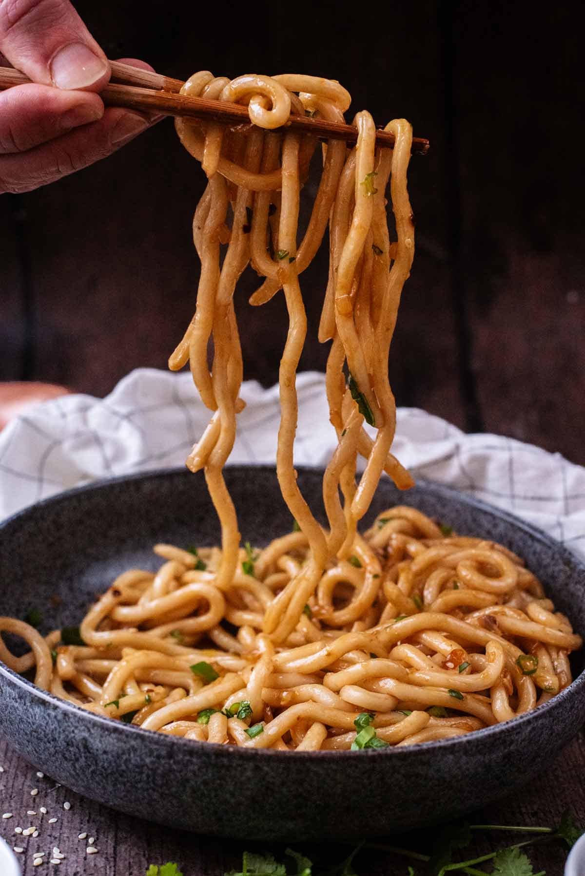A hand holding chopsticks lifting noodles from a bowl.