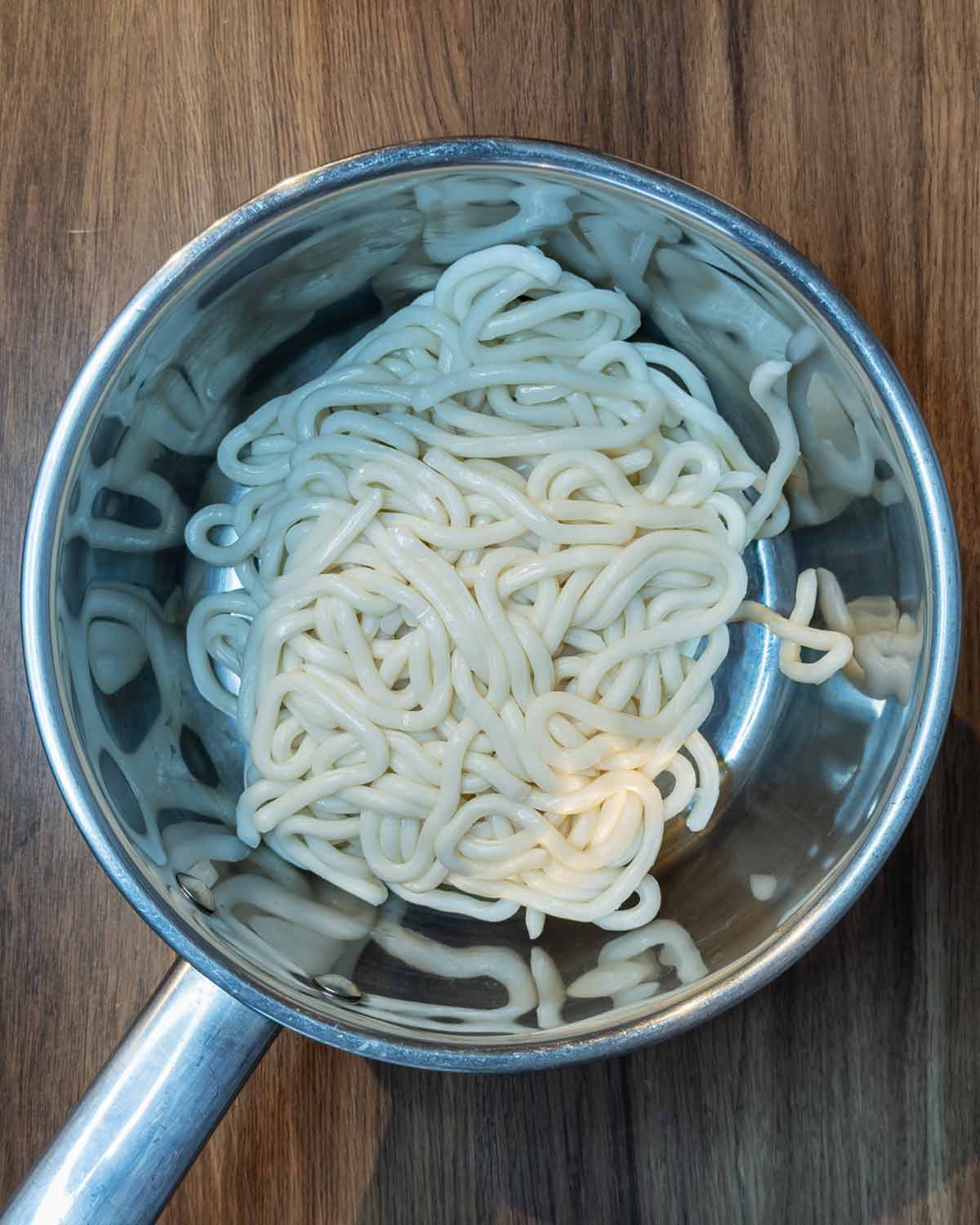 Uncooked udon noodles in a saucepan.