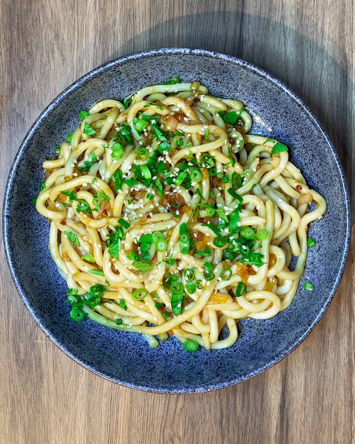 A bowl of noodles in a sauce topped with spring onions and chopped coriander.