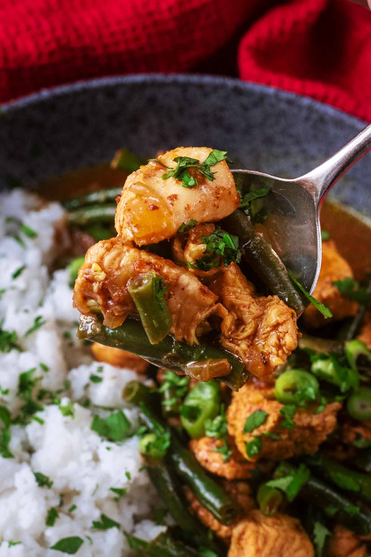 A spoon lifting some chunks of chicken and some green beans from a bowl of curry.