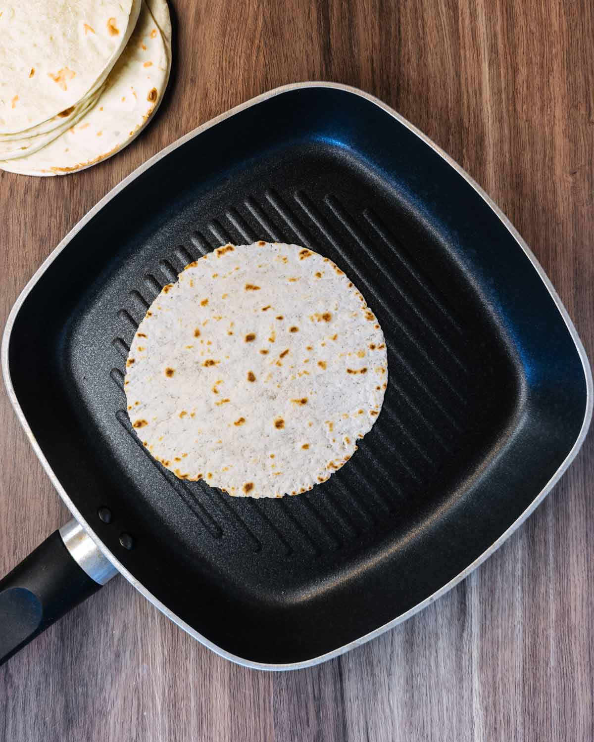 A corn tortilla dry frying in a griddle pan.
