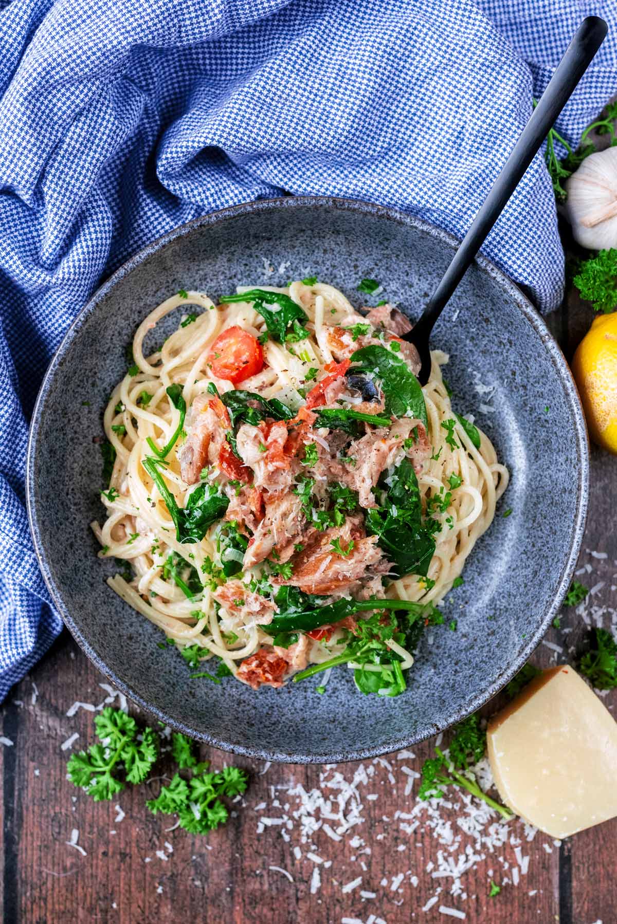 A bowl full of spaghetti mixed with flaked mackerel, tomatoes and spinach.