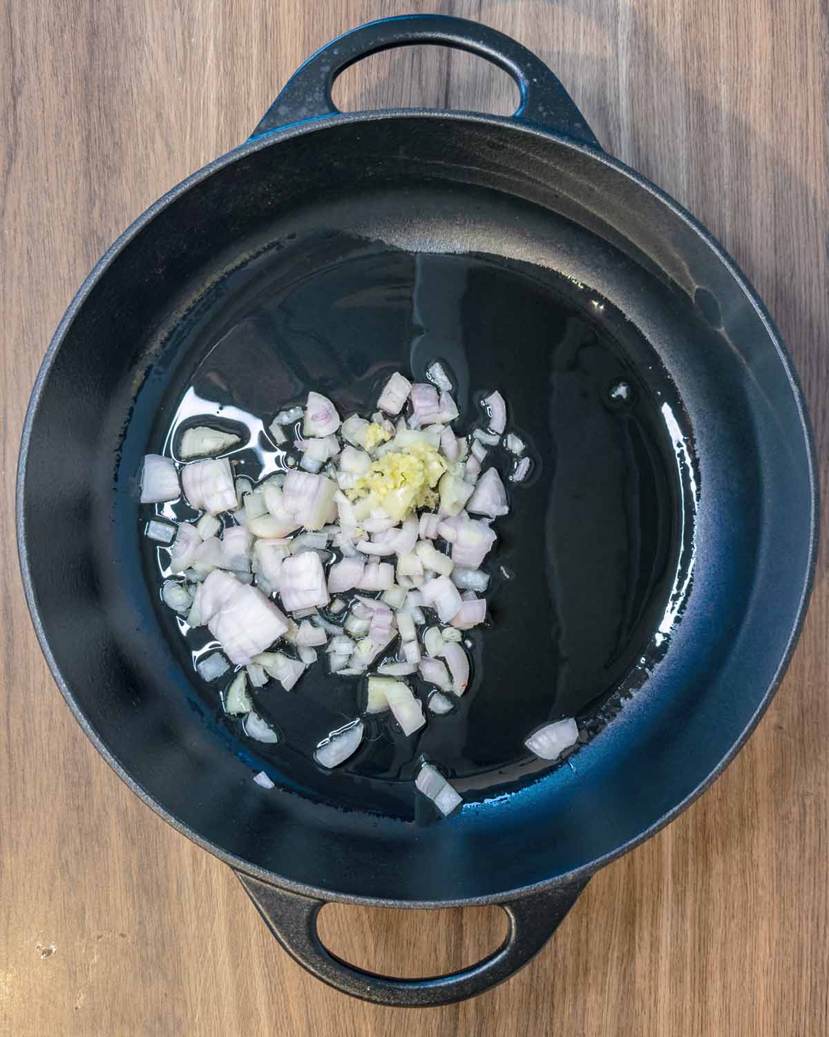 Chopped shallots cooking in some oil in a large black pan.