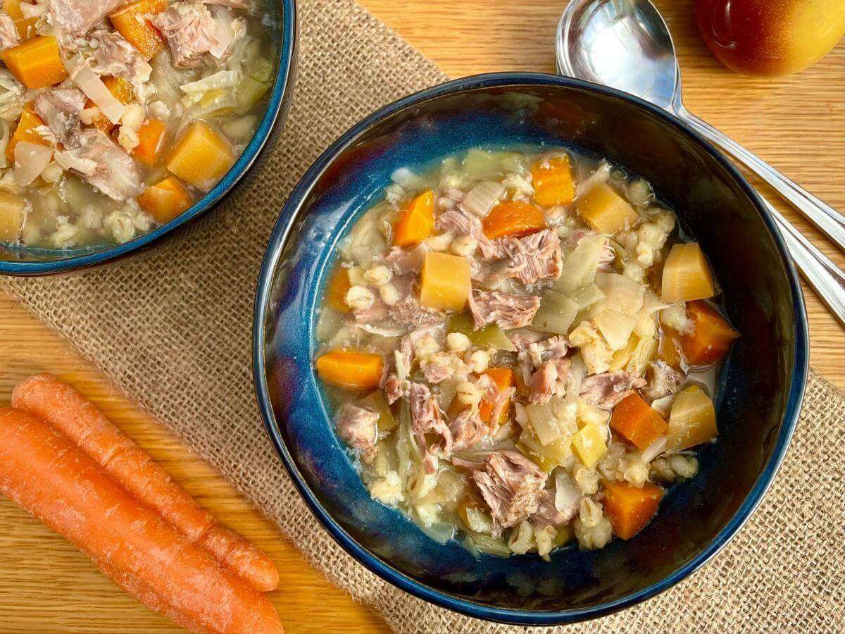 Two bowls of Scotch broth on a hessian mat with two carrots.