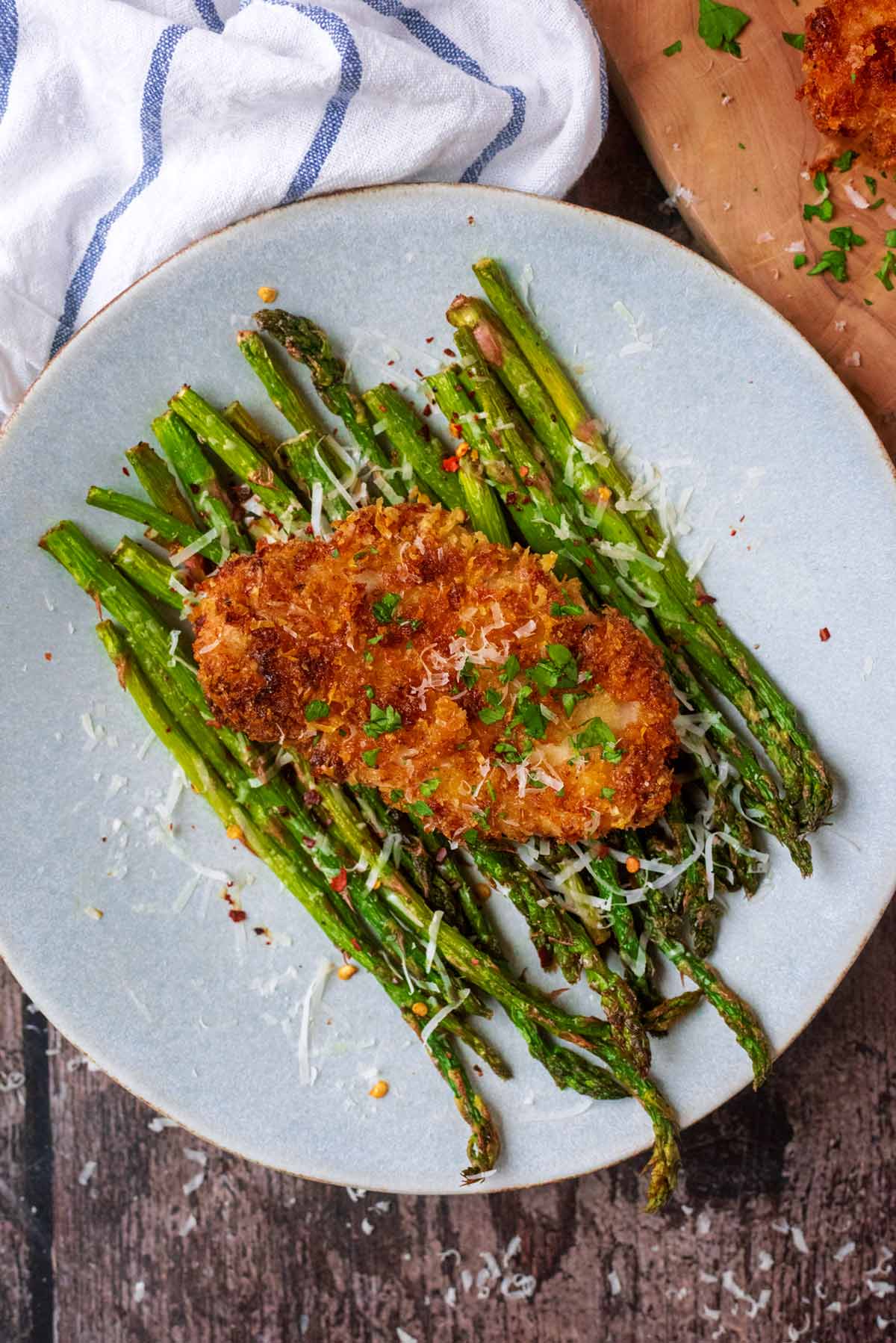 A plate of cooked asparagus with a breaded chicken breast on top of them.