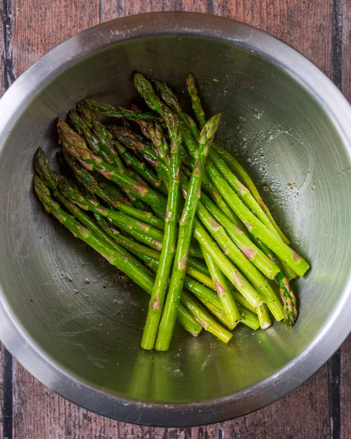 Asparagus spears in a bowl with oil, salt and pepper.
