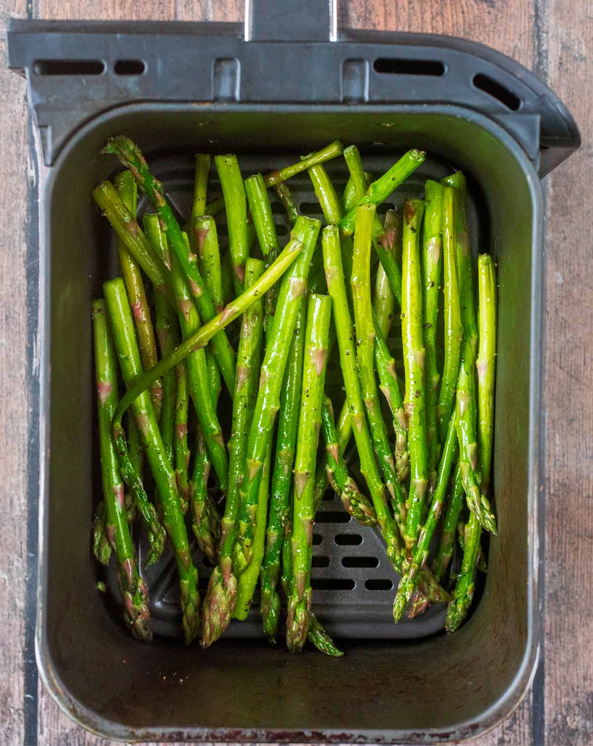 Coated asparagus in an air fryer basket.