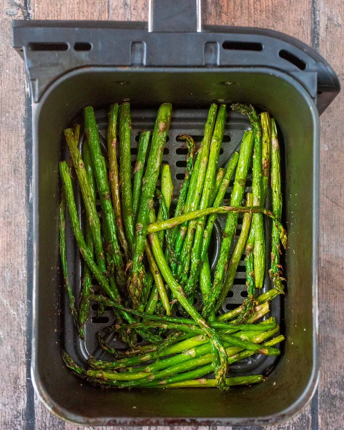 Cooked asparagus spears in an air fryer basket.