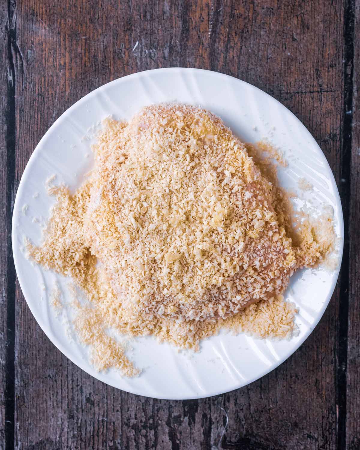 Breaded uncooked chicken breast on a plate.