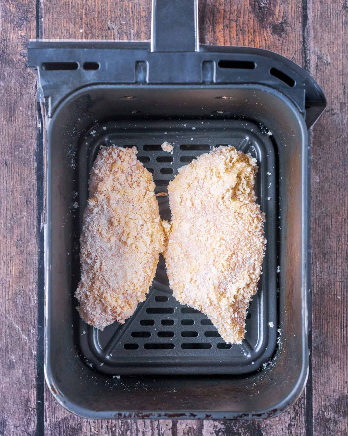 Coated chicken breasts in an air fryer basket.
