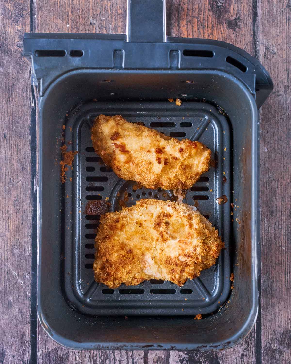 Cooked breaded chicken breasts in an air fryer basket.