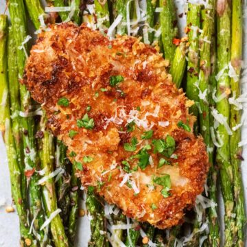 Air fryer parmesan crusted chicken breast on a bed of cooked asparagus.