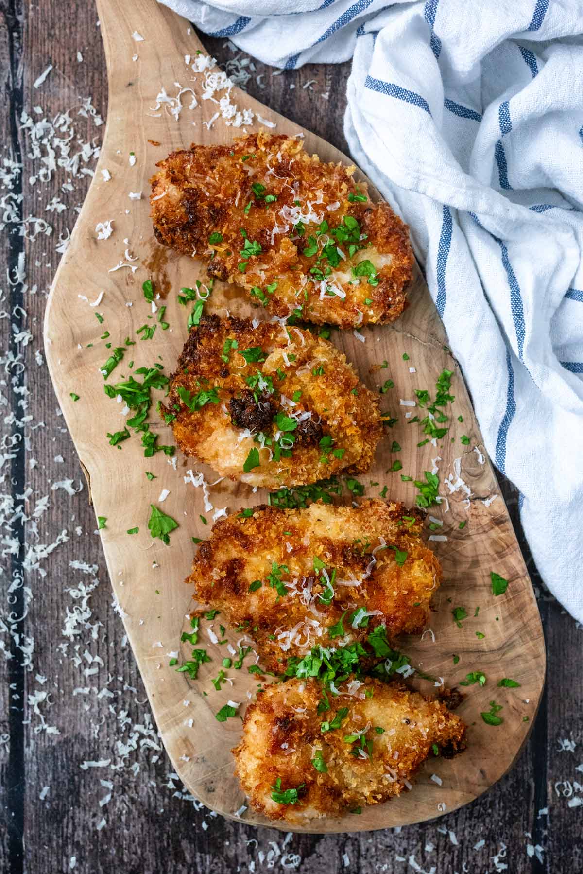 Four breaded chicken breasts on a wooden serving board.