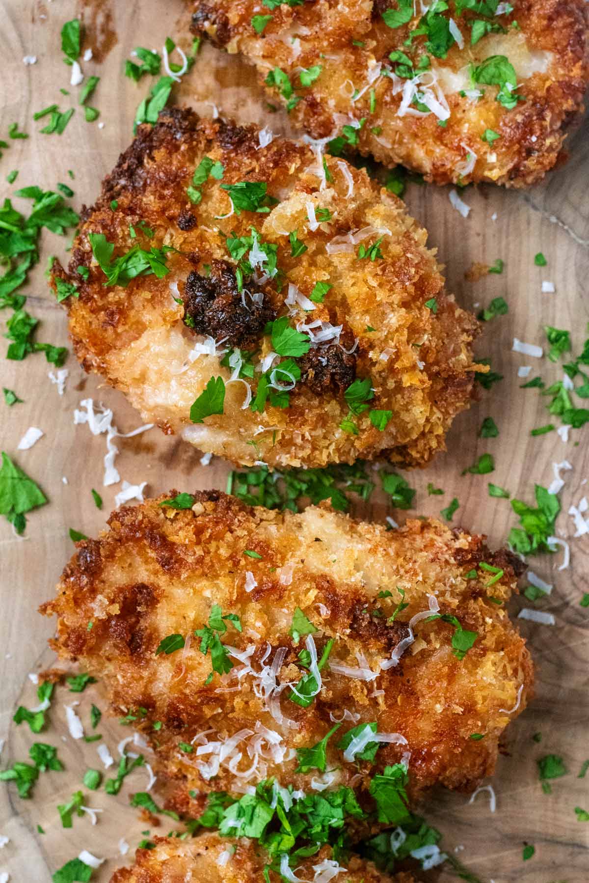 Golden breadcrumb coated chicken breasts with chopped herbs scattered over them.