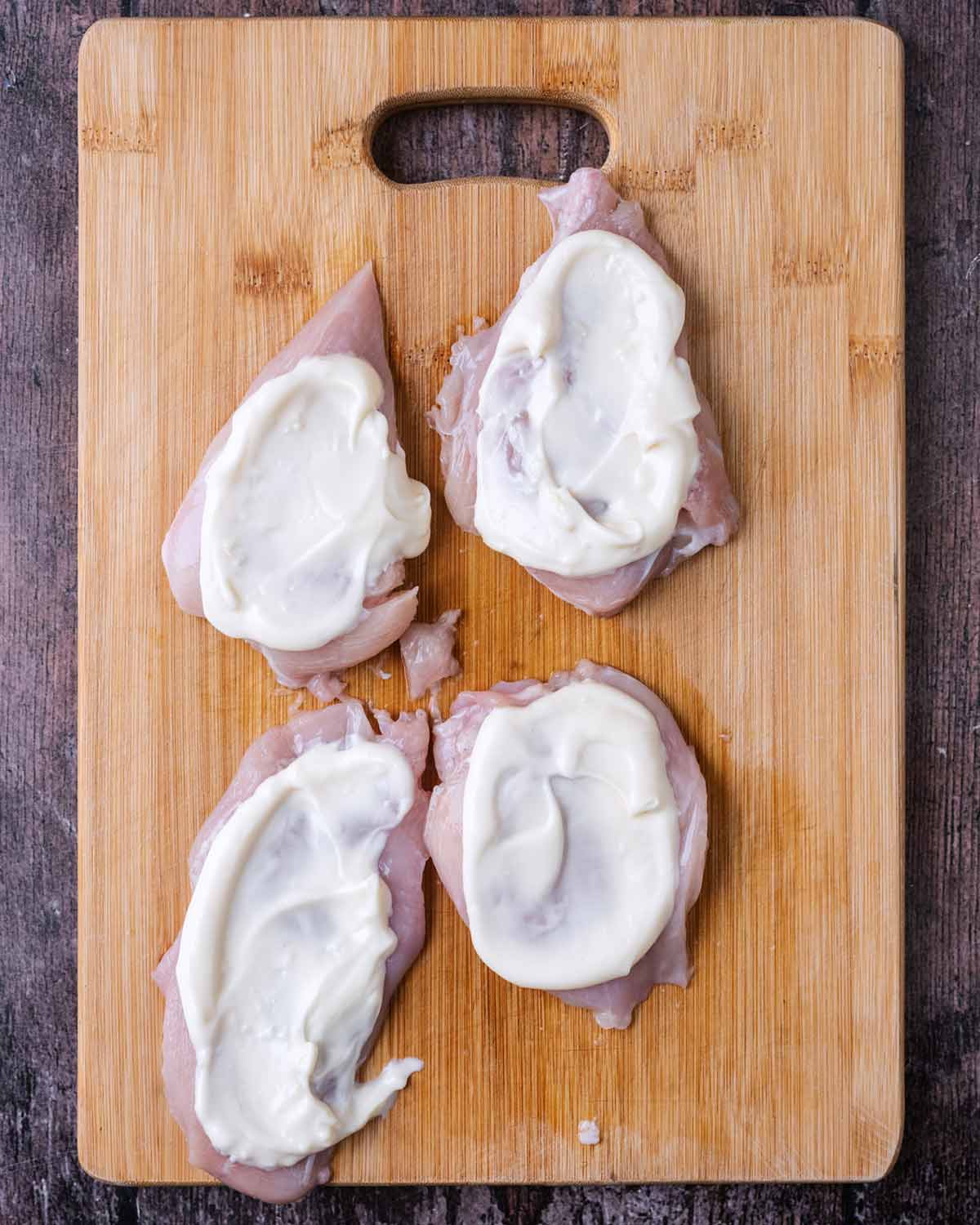 Four chicken breasts with mayonnaise spread over them.