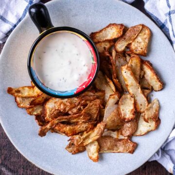A plate of air fryer potato peels with a pot of creamy dip.