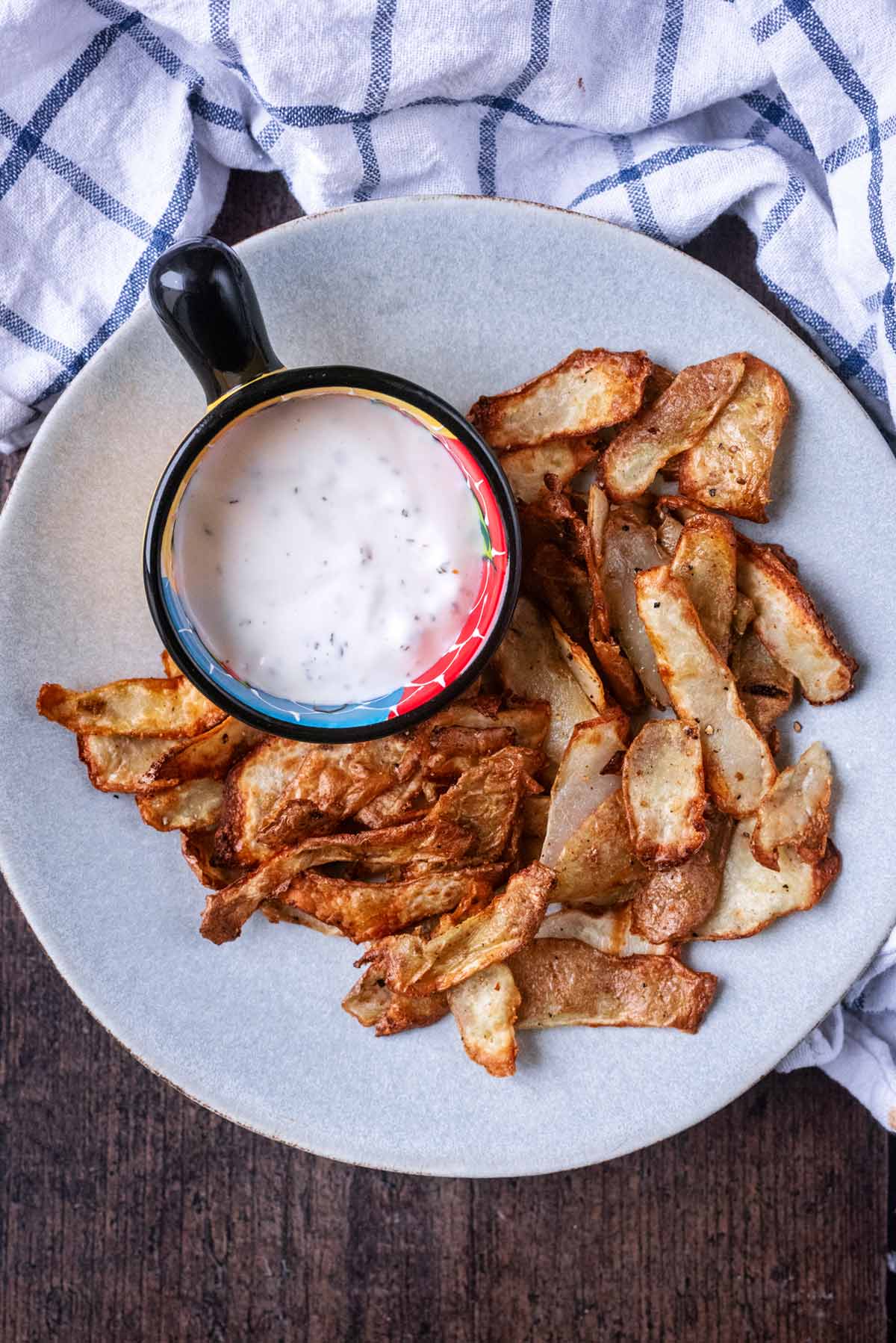 Crispy potato peelings on a plate with a small bowl of white dip.