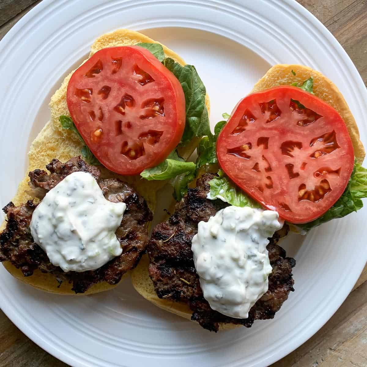 Two lamb patties on burger buns with tzatziki, tomato slices and lettuce.