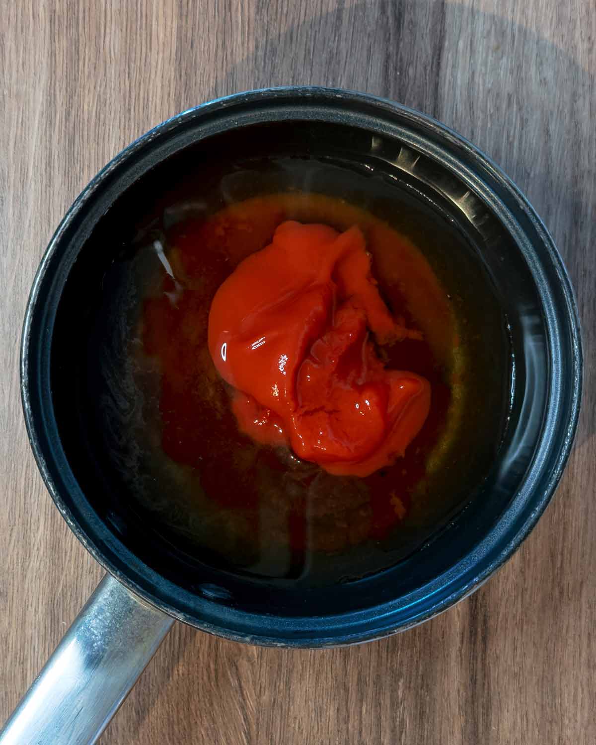A small saucepan containing water, hoisin, ketchup and tomato puree.