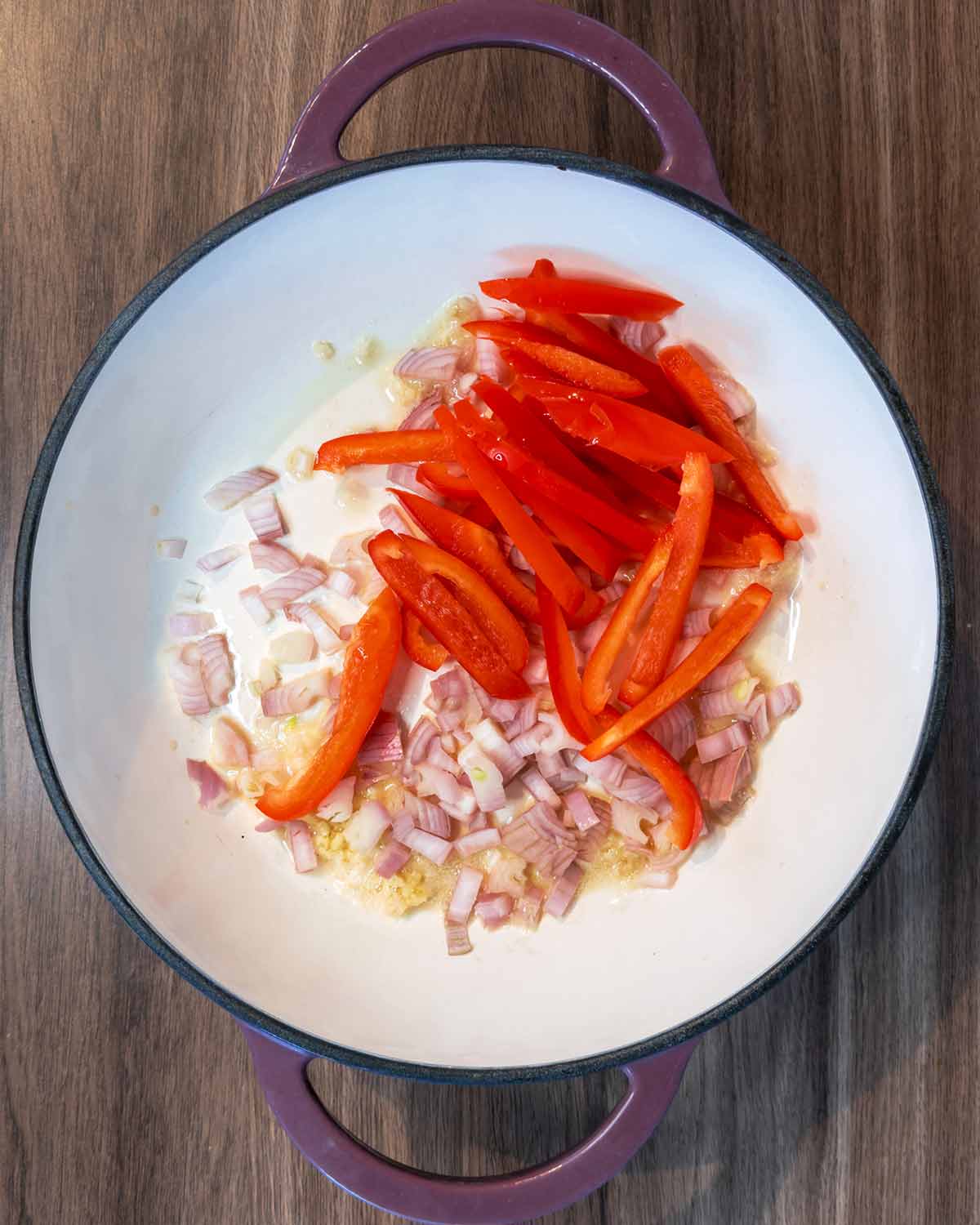 A large pan with chopped shallots and sliced red peppers cooking in it.