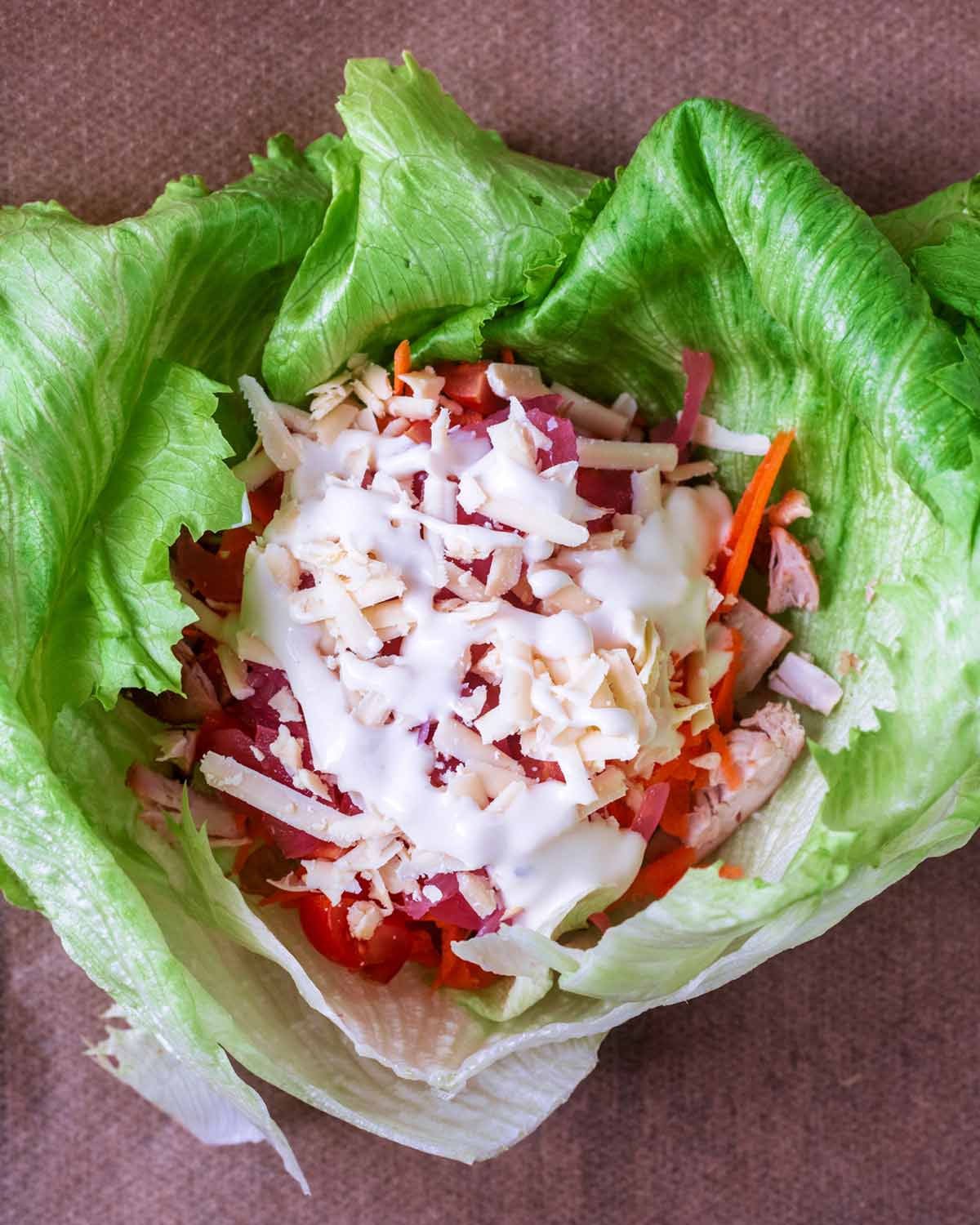Salad items, diced chicken, cheese and sauce inside the lettuce leaves.