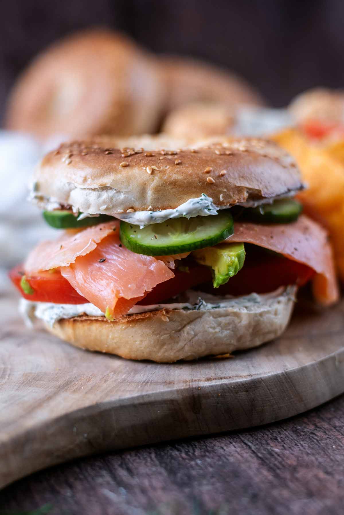 A bagel filled with cream cheese, slices of salmon, tomato, cucumber and avocado.