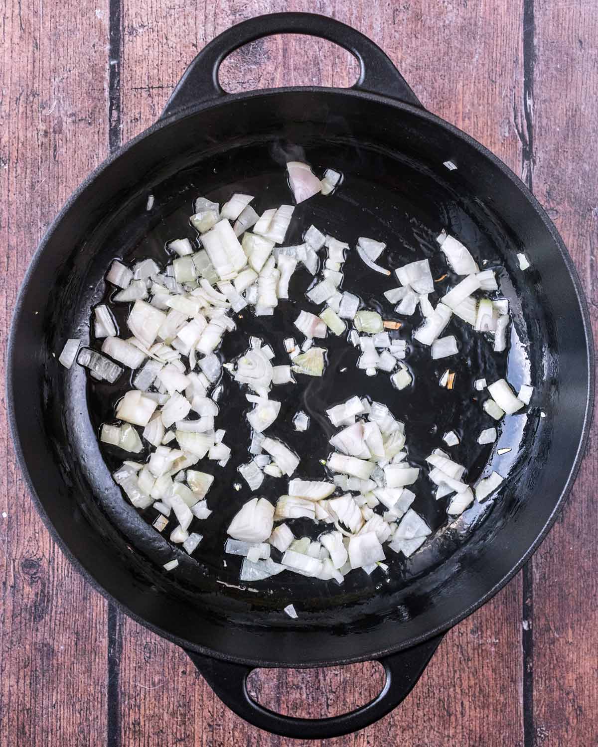 Diced shallots cooking in oil in a large black pan.