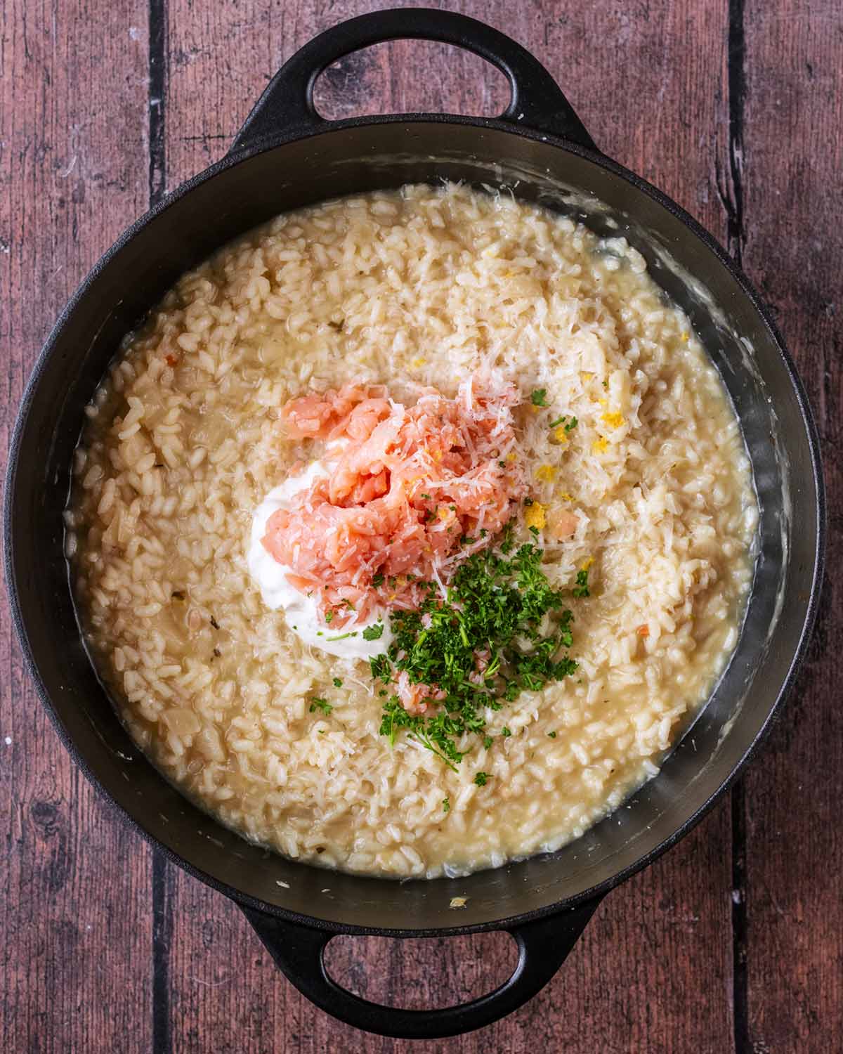 Cooked risotto with cream, salmon, cheese and herbs on top of it.