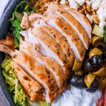 A sliced air fryer Greek chicken breast next to olives and lettuce.