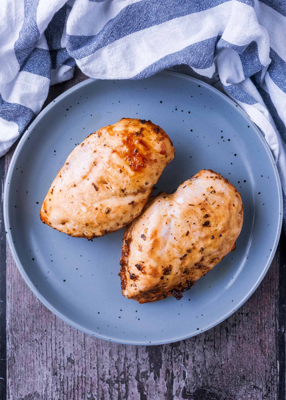 Two cooked chicken breasts on a round grey plate.