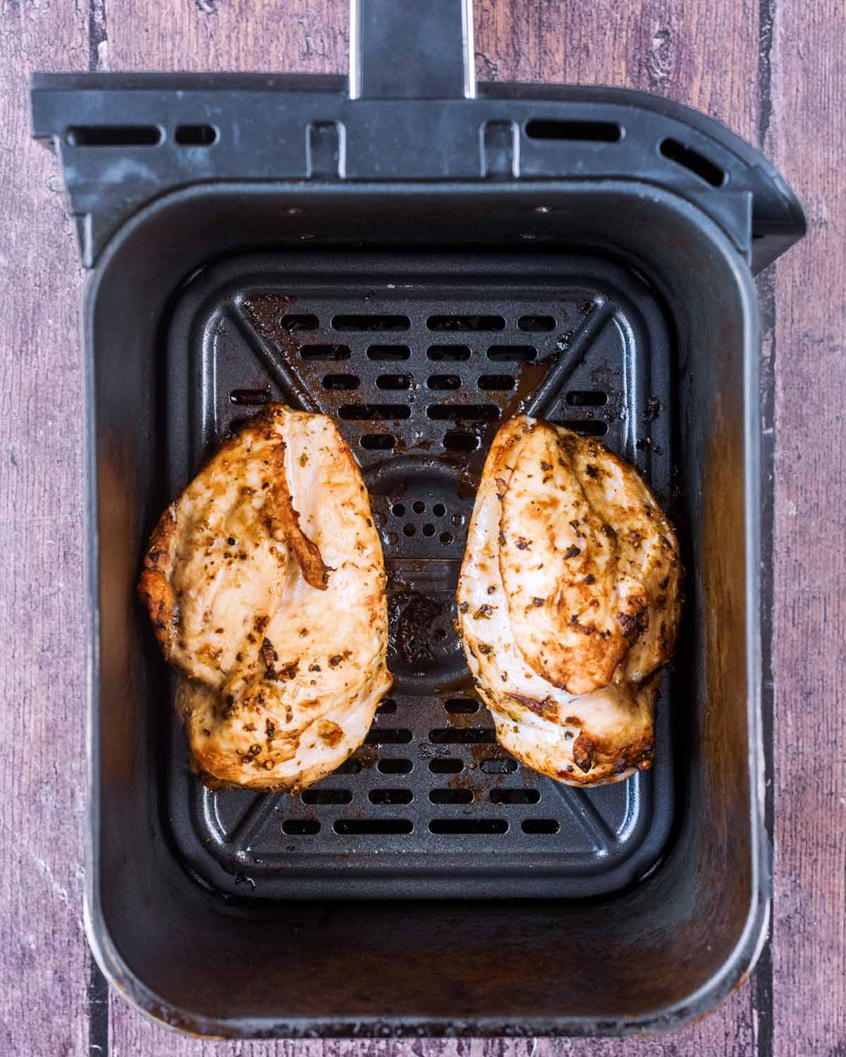 Cooked chicken breasts in an air fryer basket.