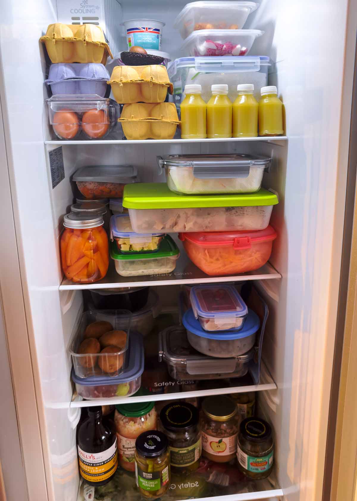 A tall fridge with shelves full of containers full of prepared fruit and vegetables.