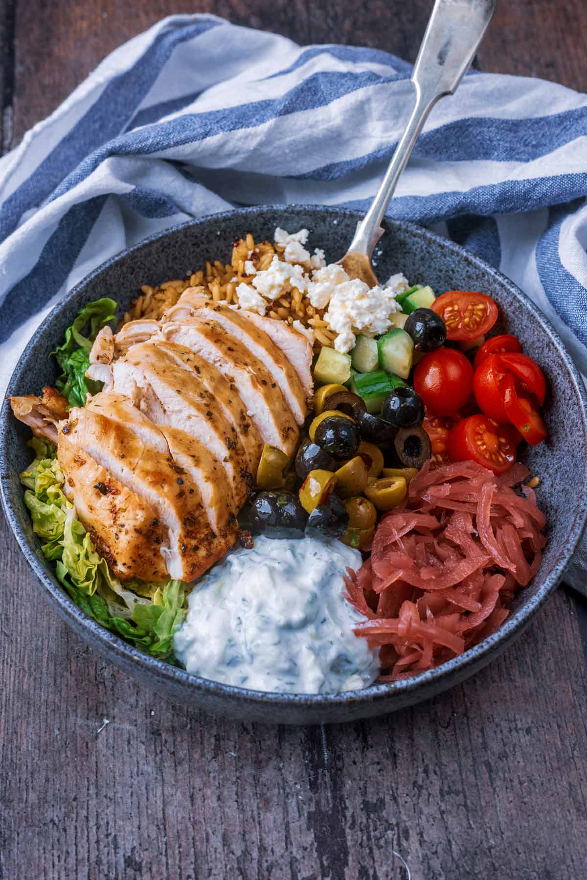 A bowl of sliced chicken and salad in front of a striped towel.