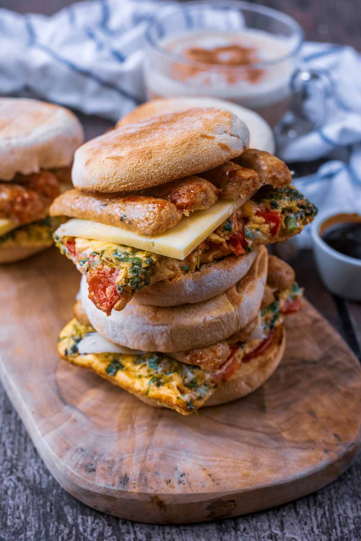 Breakfast sausage and egg muffins stacked up on a wooden board.