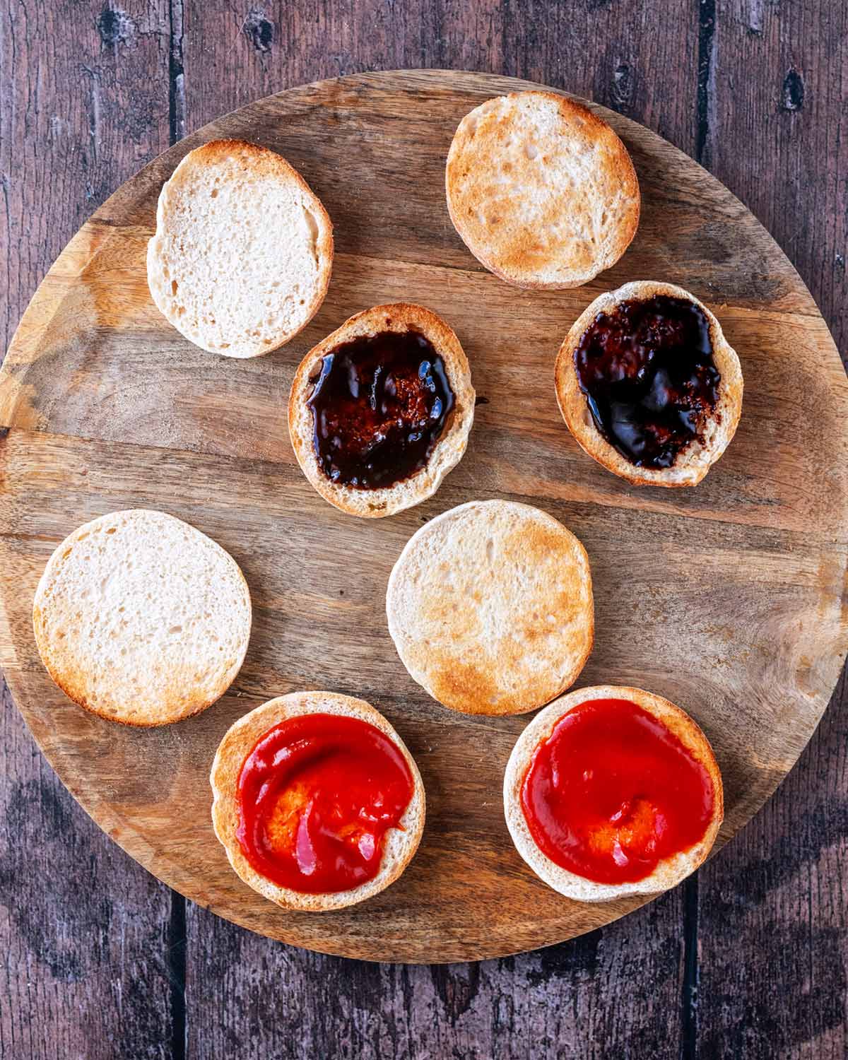 Eight toasted muffin halves, two with ketchup two with barbecue sauce.