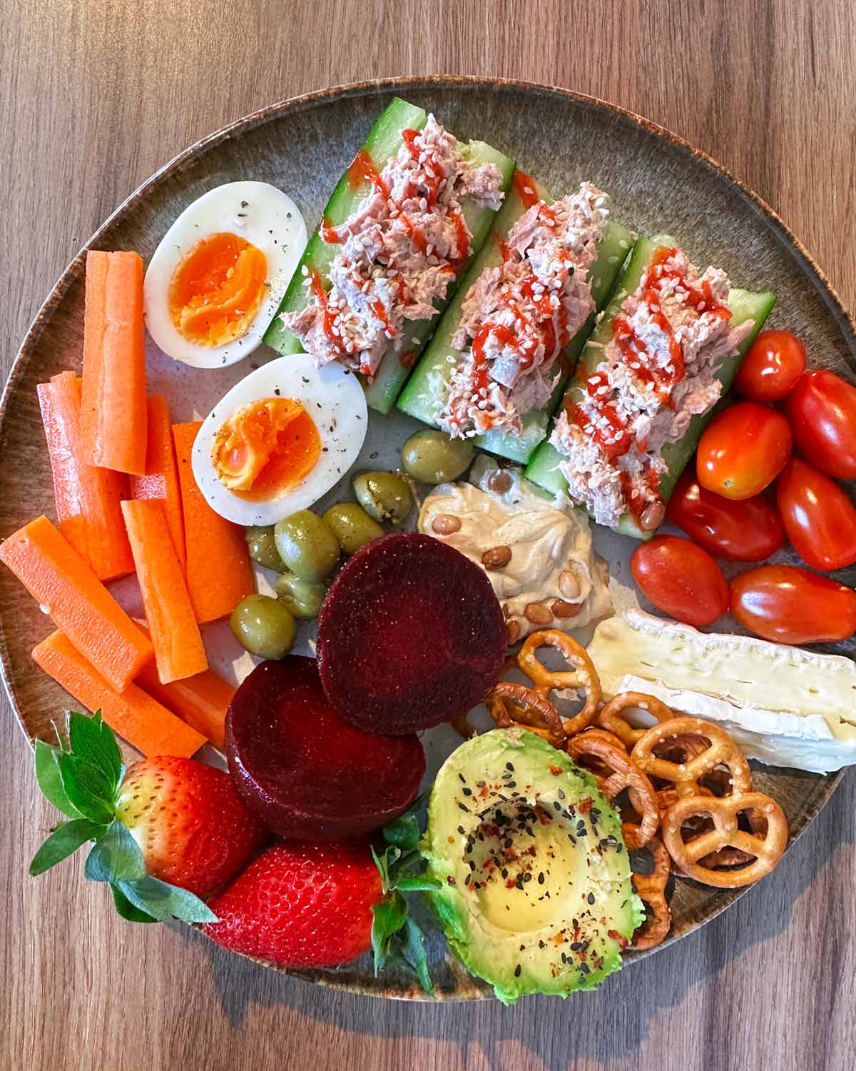 A plate of carrot battens, boiled egg, tuna mayo, beetroot, pretzels and half an avocado.