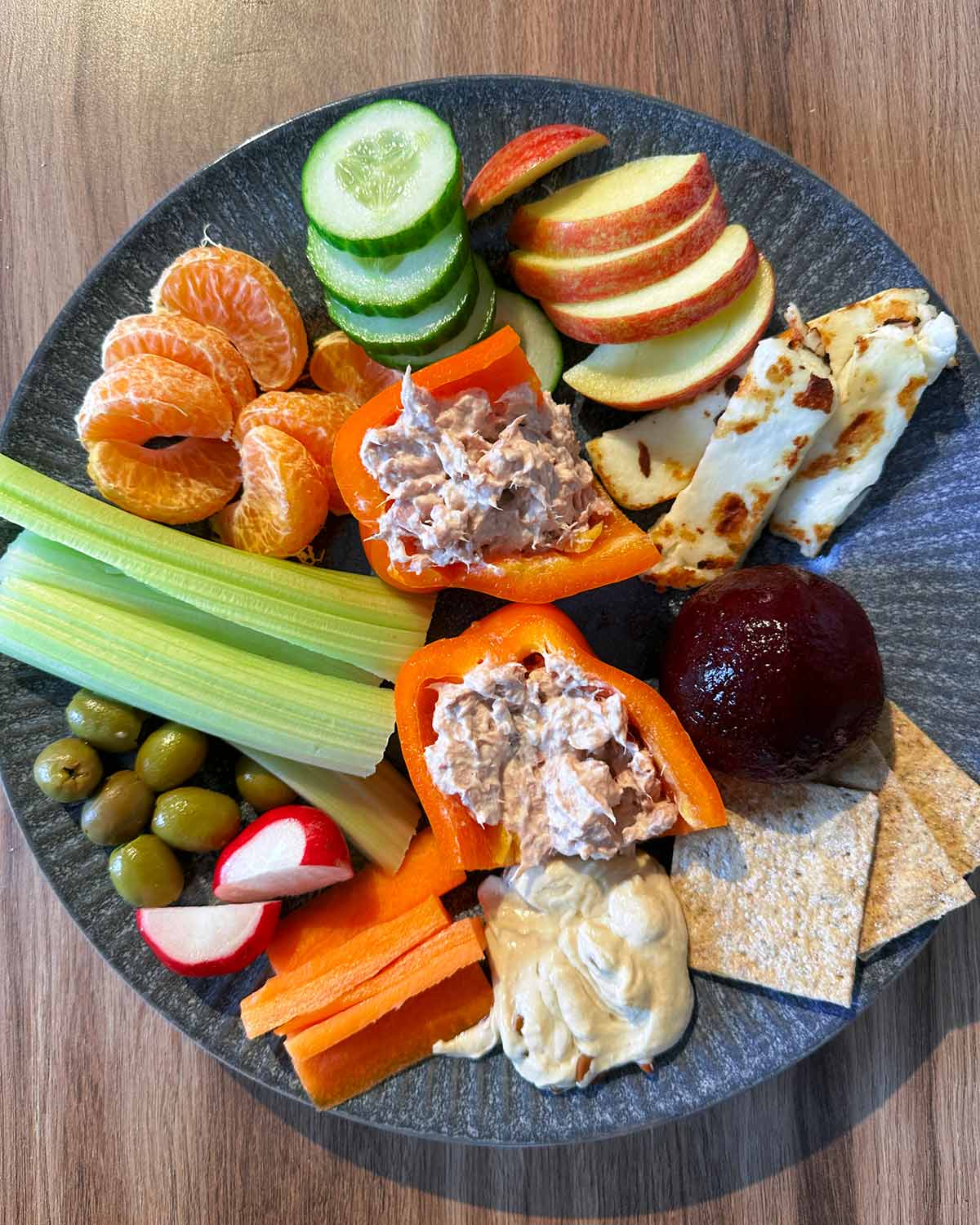 A plate of tuna stuffed peppers, celery, halloumi, crackers, humus, beetroot, olives and orange segments.