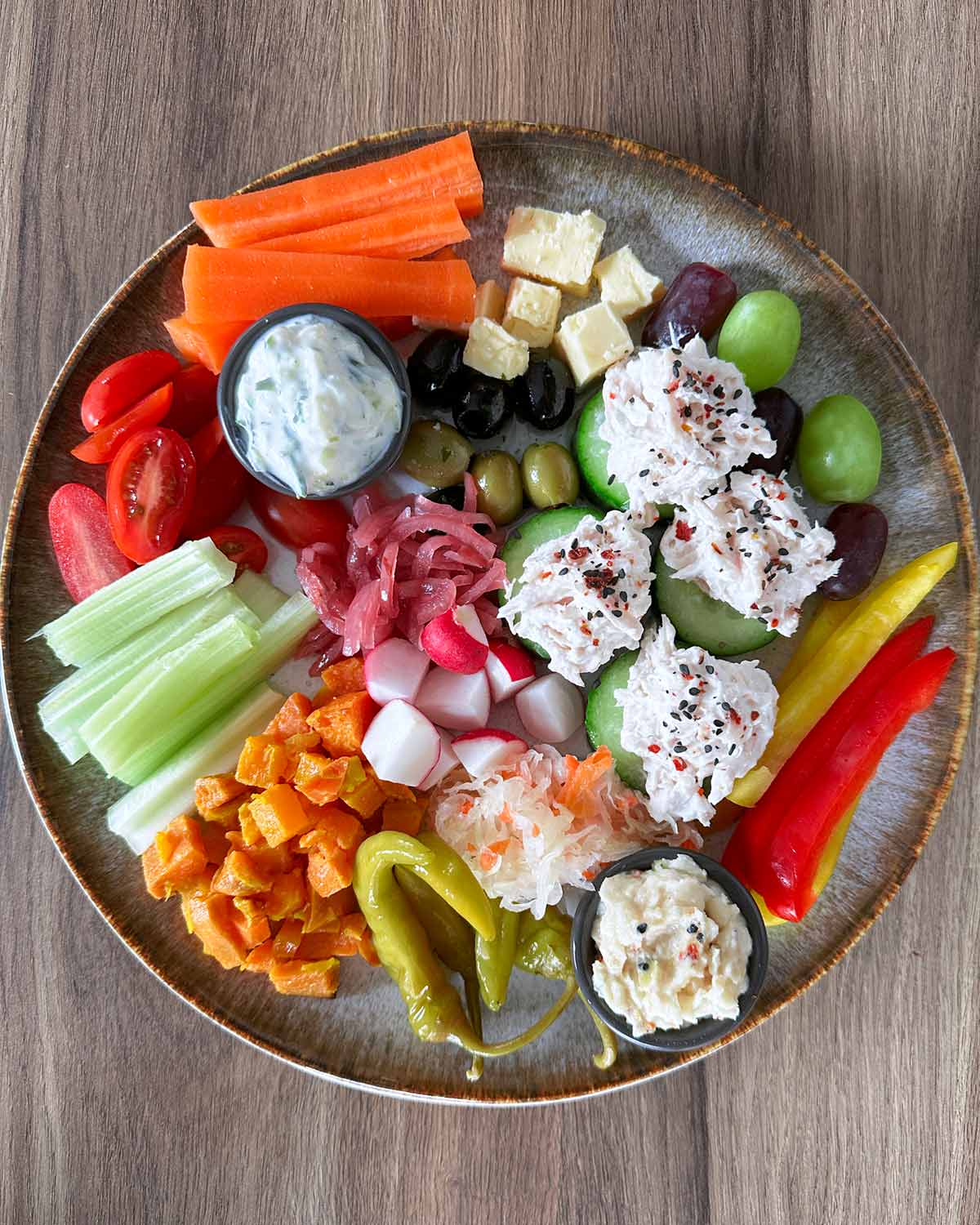 A plate with tuna may, cucumber, carrots, celery, peppers, sauerkraut, cheese and dips.