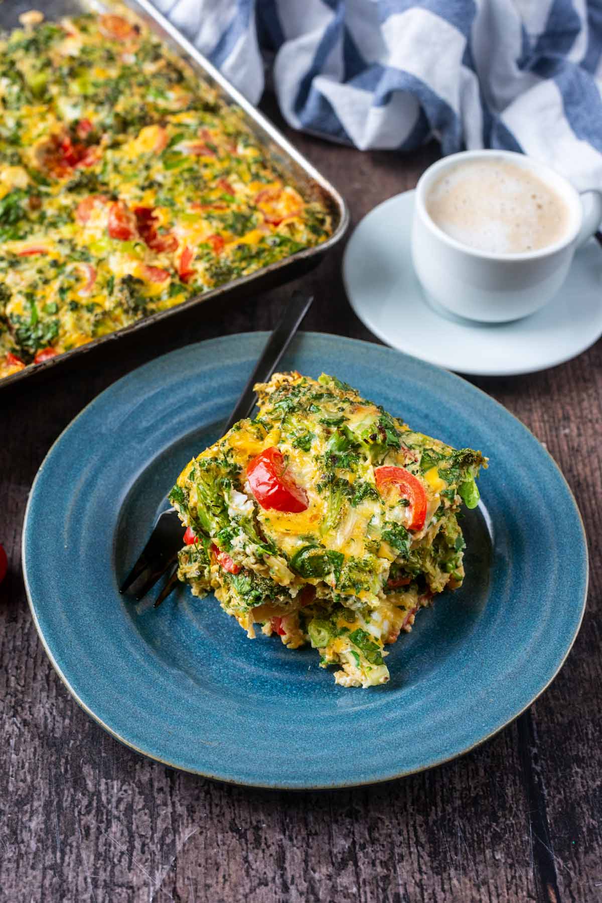 Sliced egg bake on a plate next to a pan of the bake and a cup of coffee.