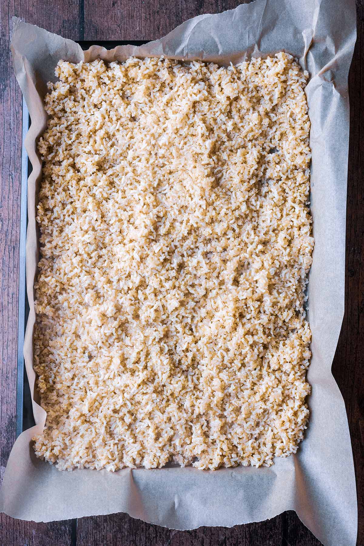 A lined baking tray with rice and quinoa cooling on it.