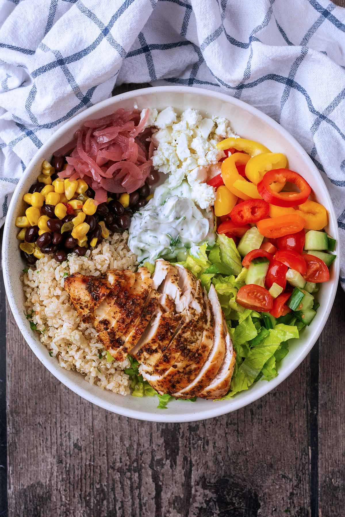 A bowl of cooked sliced chicken, rice, quinoa, vegetables and cheese.