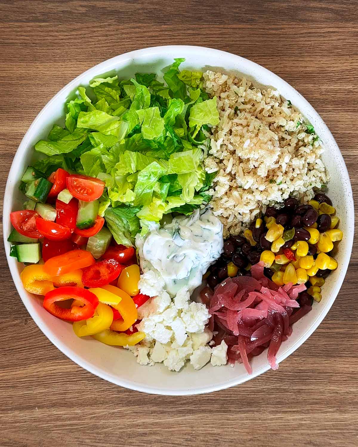 A bowl containing lettuce, rice, corn, beans, peppers and cheese.