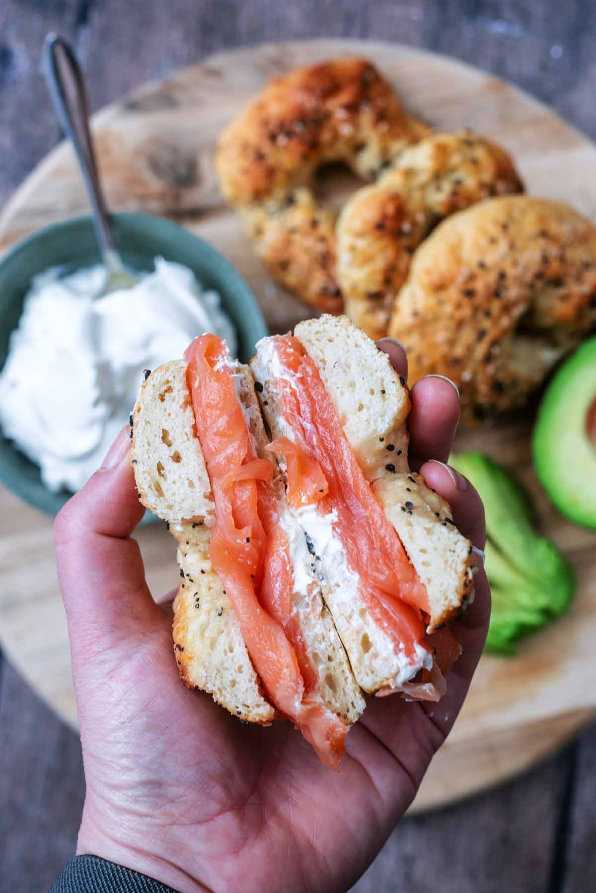 A hand holding a sliced open salmon bagel.