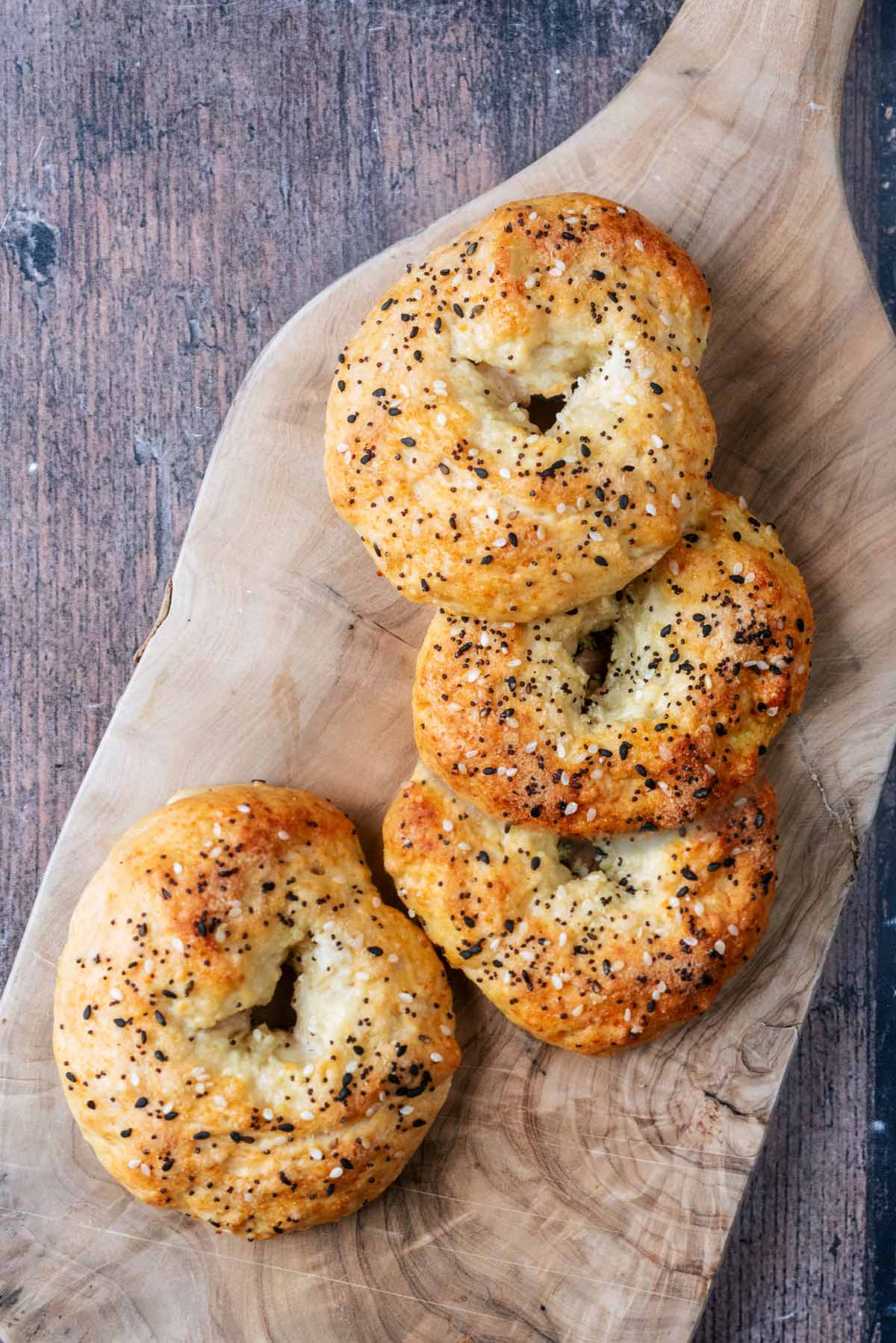 Four bagels topped with sesame seeds on a wooden serving board.