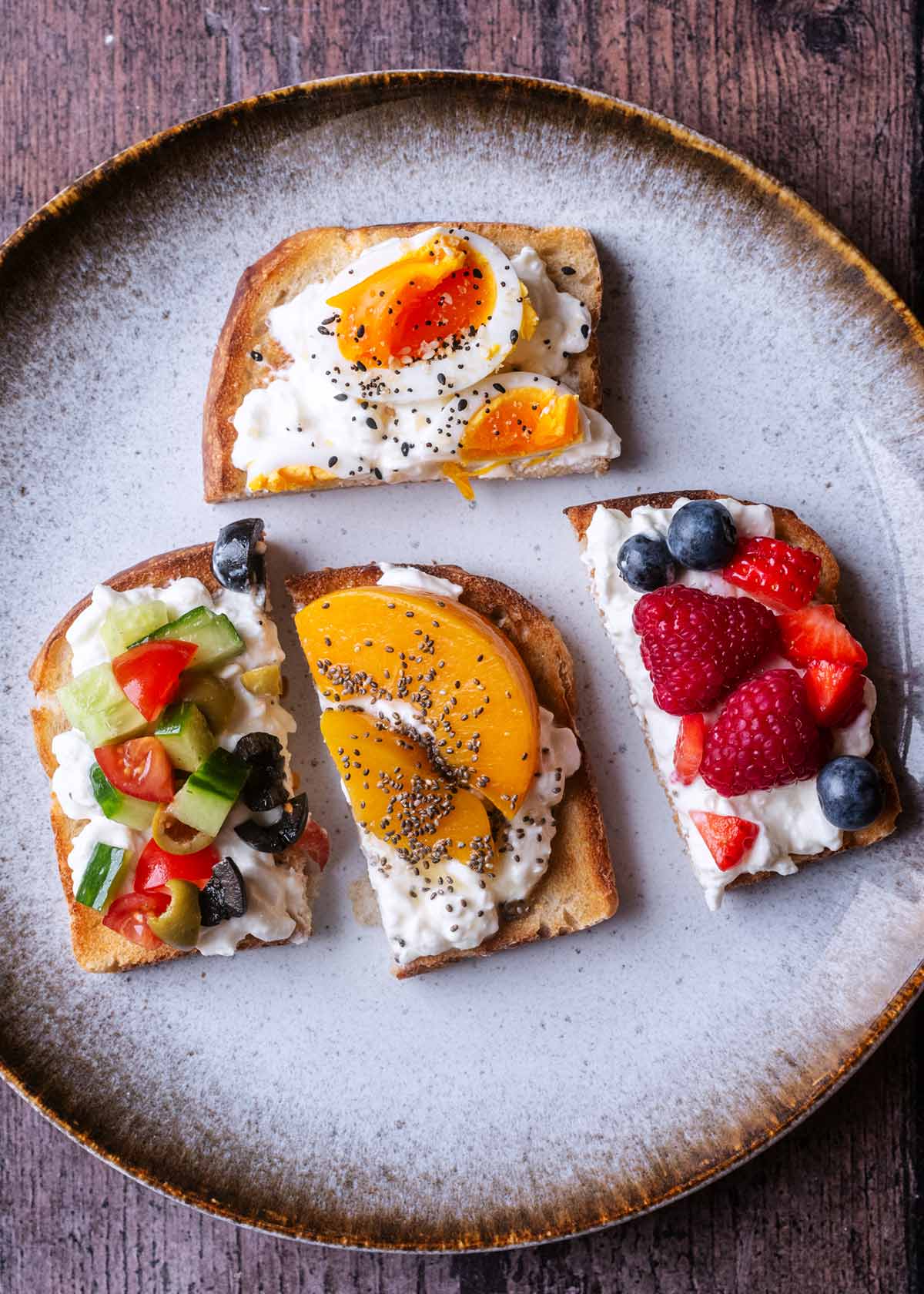 Four half slices of toast on a plate, each with cottage cheese and a different topping.
