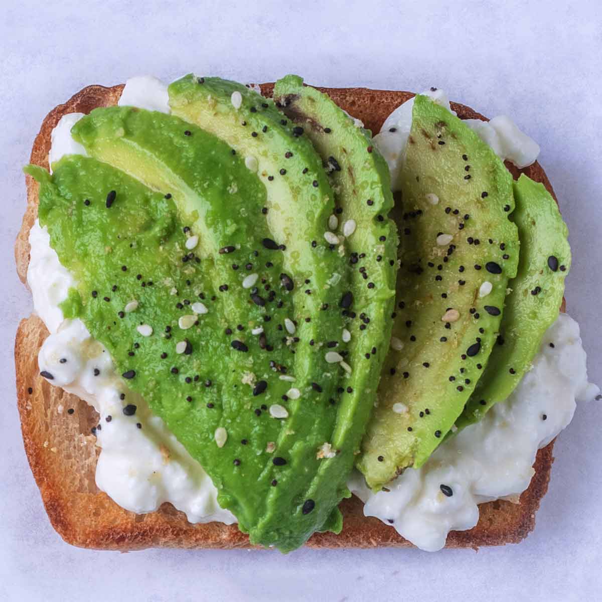 Slices of avocado and seasoning on top of cottage cheese on toast.