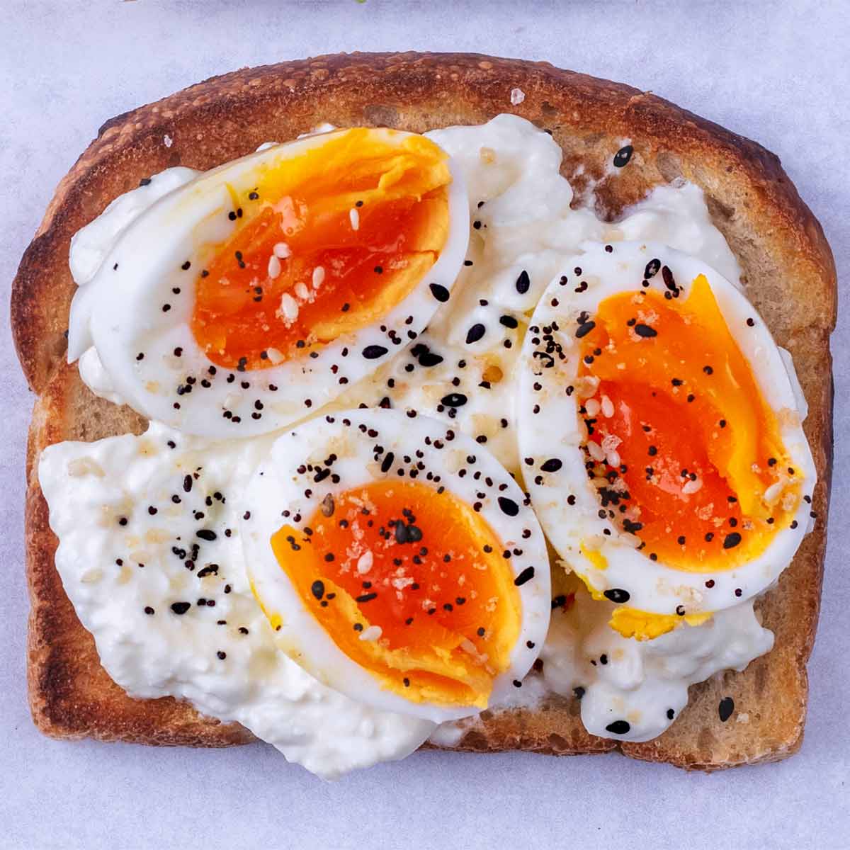 Sliced boiled eggs and seasoning on top of cottage cheese on toast.