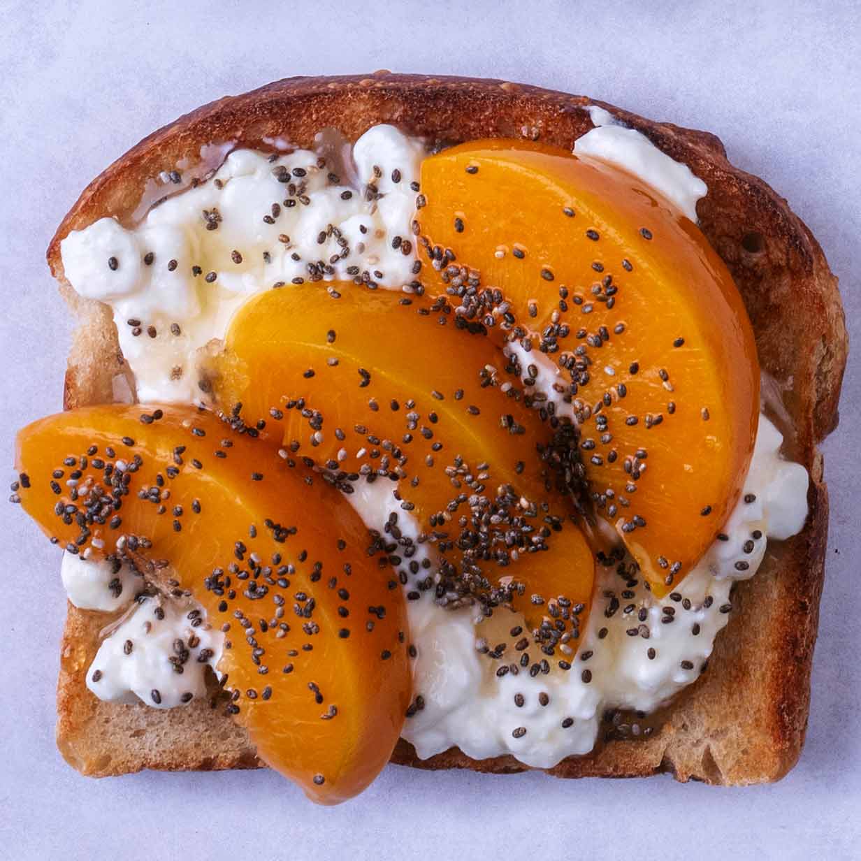 Slices of peach and chia seeds on top of cottage cheese on toast.