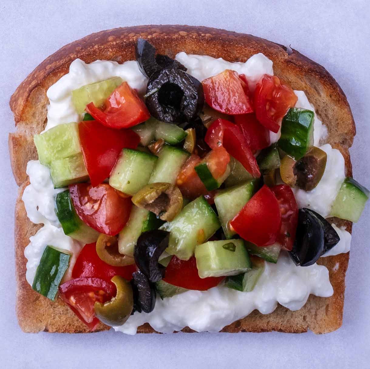 Chopped tomato, cucumber and olives on top of cottage cheese on toast.