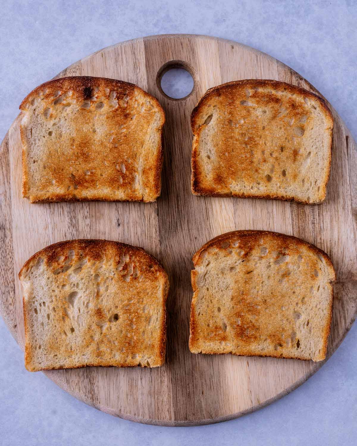 Four slices of toast on a round wooden board.